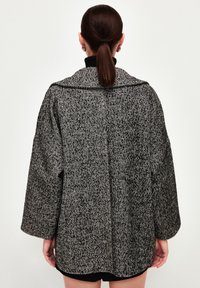 Mantel im Fischgratmuster in Schwarz und Weiß, mit Kragen, lockerer Silhouette und strukturiertem Stoff. Kurzärmel und gerader Saum.
