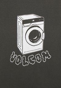 Maglietta nera con una grafica di una lavatrice disegnata a mano in bianco sopra il testo "VOLCOM" scritto in un carattere giocoso e rotondo.