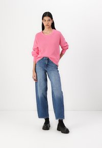 Rosa ribbet genser med bred halslinje, kombinert med lyseblå høy liv straight-leg jeans og svarte kraftige ankelstøvler.
