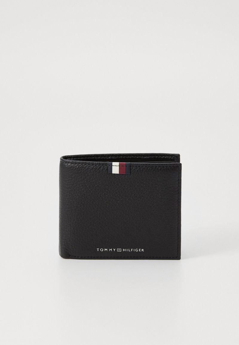 Portefeuille en cuir noir avec finition texturée, design pliable en deux, et un petit accent de drapeau multicolore. Présente le nom de la marque imprimé.