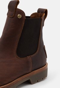 Καφέ δερμάτινη μπότα μέχρι τον αστράγαλο με ελαστική πλευρική επένδυση και ελαφριά ραφή. Διαθέτει καφέ καουτσούκ σόλα με ανθεκτική επιφάνεια. Διακοσμητικό λογότυπο από ορείχαλκο.