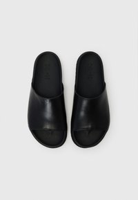 Svarte lær slid sandaler med åpen tå-design, glatt overflate og teksturert svart innersåle. Sålen har en lett krumning.