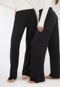 Pantaloni neri a gamba larga con vita elasticizzata, realizzati in un materiale liscio e elastico, caratterizzati da un design fluido e dettagli minimi.