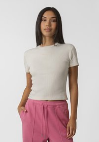 Haut beige à manches courtes en côtes avec un col rond. Tissu doux, design ajusté. Associé à un pantalon de jogging rose avec cordon de serrage et poches latérales.