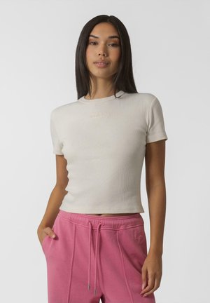 Haut beige à manches courtes en côtes avec un col rond. Tissu doux, design ajusté. Associé à un pantalon de jogging rose avec cordon de serrage et poches latérales.