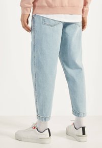 Vaqueros de mezclilla azul claro con un ajuste holgado, dobladillos doblados y bolsillos traseros, combinados con zapatillas blancas y calcetines grises.