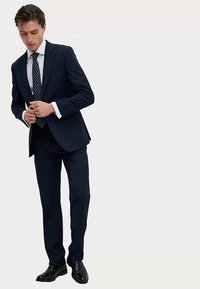 Navyblauw pak met een slank ontwerp, gecombineerd met een wit overhemd en een gestreepte stropdas. Gladde textuur, subtiele glans en gepolijste zwarte schoenen.