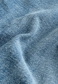 Gros plan sur un tissu en denim bleu clair montrant une texture détaillée et un motif de tissage diagonal avec des plis subtils.
