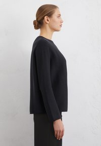 Schwarzes Langarmshirt mit Rundhalsausschnitt und geradem Schnitt. Aus strukturiertem Stoff gefertigt, mit minimalen Nähten und klaren Linien.