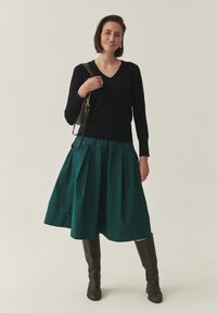 Must v-kaelusega kampsun, millele on lisatud roheline voltidega seelik, mis ulatub just põlve alla. Pruunid põlveni ulatuvad saapad ja risti üle keha kantav käekott täiendavad välimust.