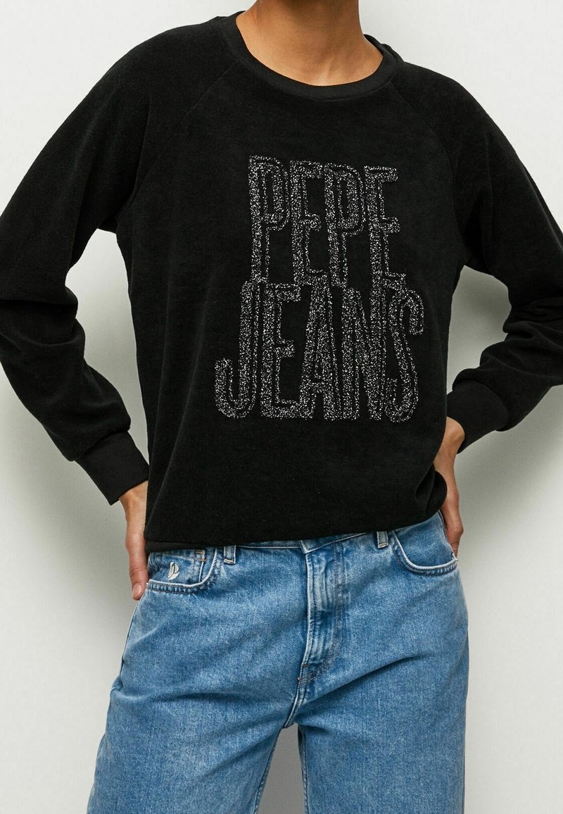 Sweat-shirt noir avec « PEPE JEANS » en paillettes argentées, doté d'un col rond et de manches raglan, associé à un jean en denim bleu clair.
