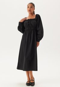 Zwart midi-jurkje met lange pofmouwen, een vierkante halslijn en een elastische taille. Gemaakt van lichte stof met een soepele textuur.