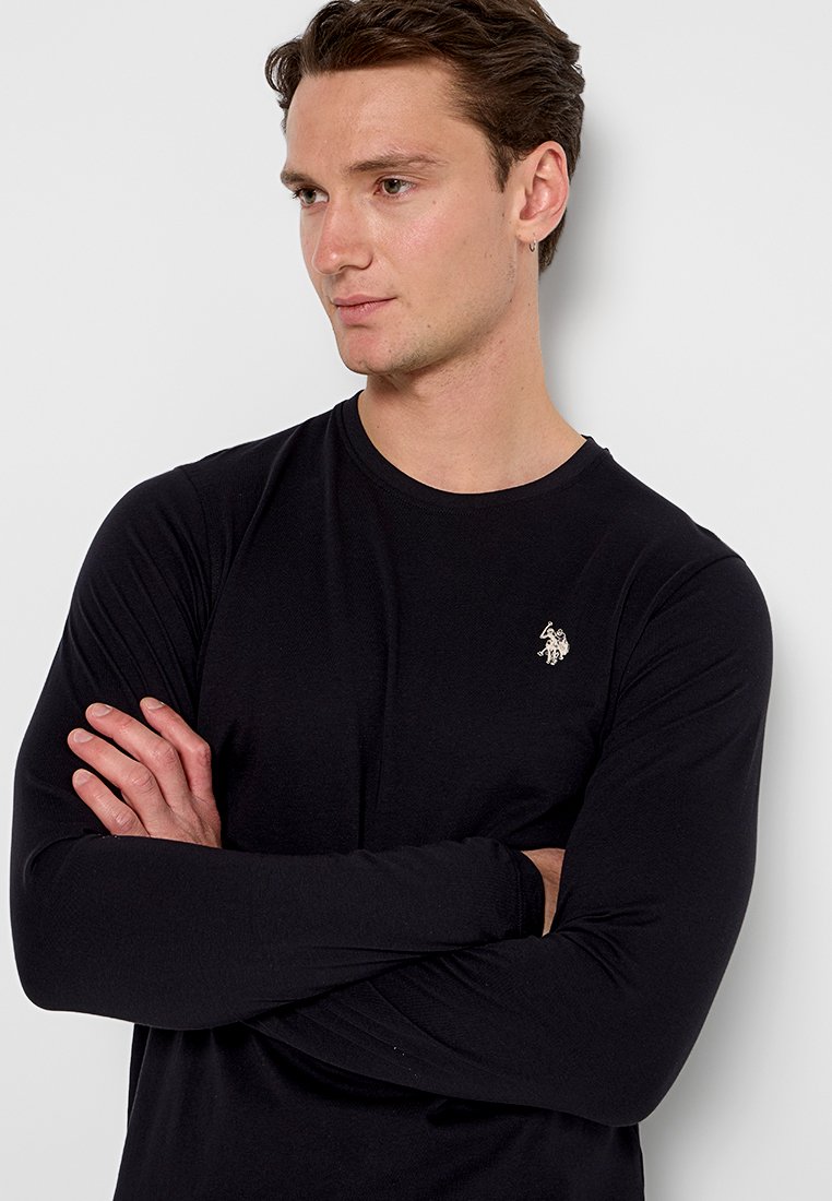 T-shirt noir à manches longues en tissu doux, arborant un logo brodé discret sur la poitrine gauche et un design ajusté.