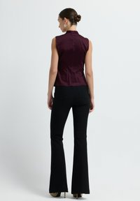 Haut sans manches bourgogne avec un col haut, en tissu lisse ; associé à un pantalon noir évasé. La vue arrière montre une silhouette ajustée et un design sur mesure.