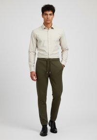 Beige knäppskjorta i kombination med mörkgröna joggerbyxor. Byxorna har en elastisk midja med dragsko. Svarta skor fulländar outfiten.