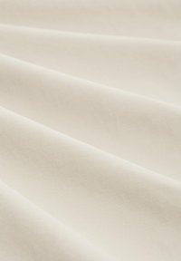 Bawełniana tkanina w delikatnym kremowym kolorze o teksturowanej powierzchni, prezentująca łagodne fałdy i gładki wygląd.