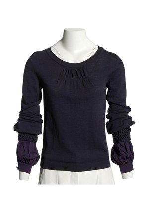 Pull bleu marine à manches longues avec des détails froncés au niveau de la poitrine et des poignets, superposé sur des manches bouffantes violet de chemise sur un mannequin blanc.