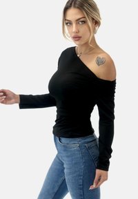 Zwarte lange mouw top met een off-the-shoulder ontwerp, gemaakt van zachte stof met geplooide details. Gepaard met blauwe jeans.