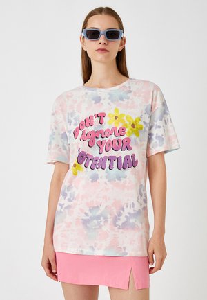 T-shirt med tie-dye i pastelfarver med korte ærmer, der har fed tekst "IGNORER DIN POTENTIALE IKKE" og gule blomsterdetaljer.