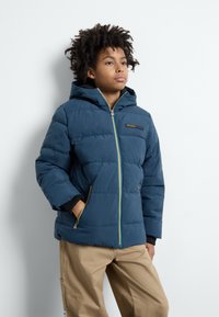 Giacca puffer blu con cappuccio, dotata di chiusura frontale con zip e tasche, zip gialla a contrasto e dettagli neri su polsini e fodera.