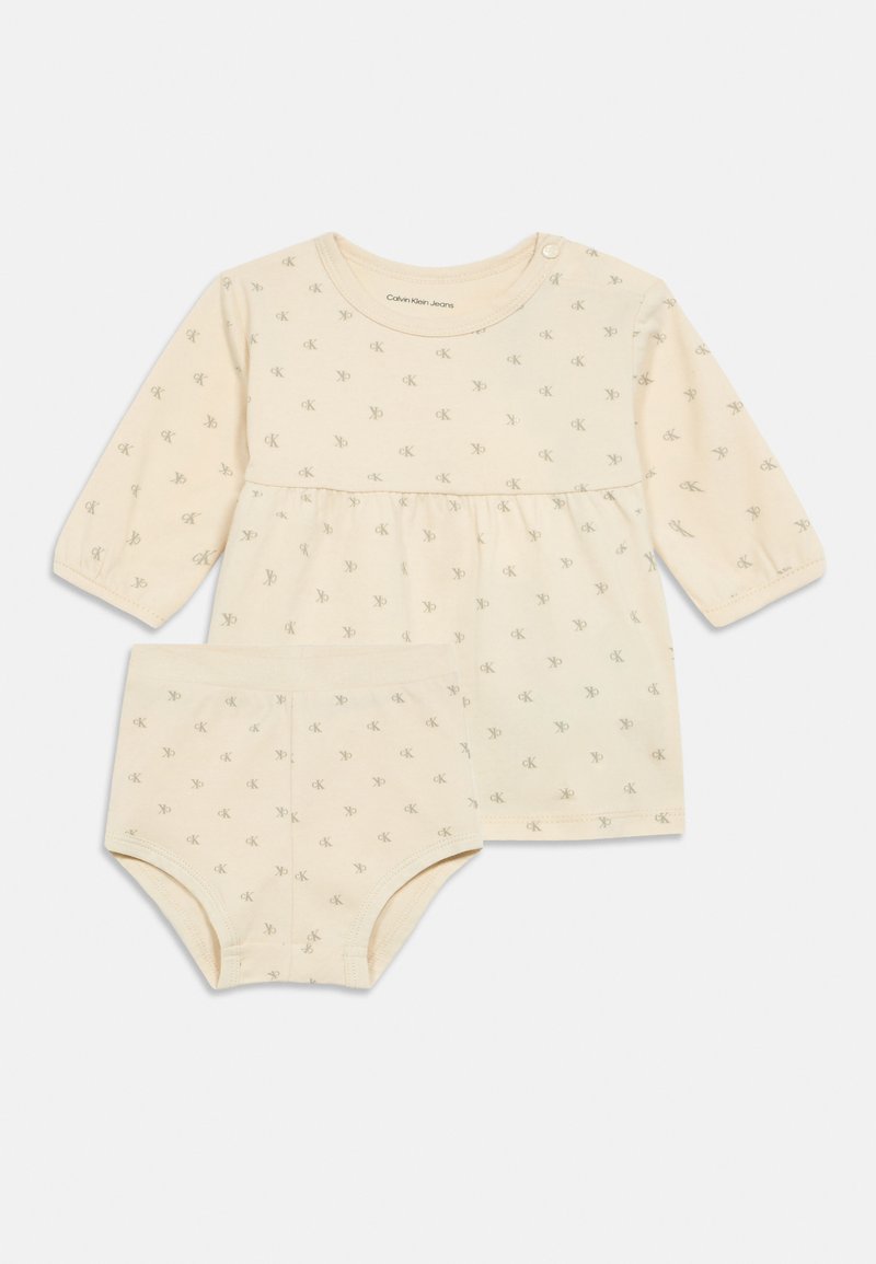 Conjunto de bebé em bege claro, com uma blusa de mangas longas com cintura franzida e calções a condizer, decorado com pequenos padrões do logo CK.