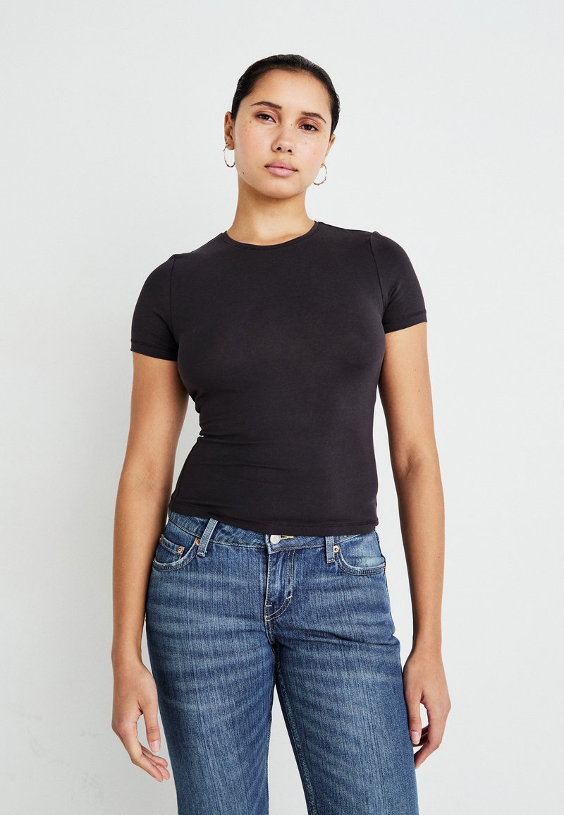 Sort tætsiddende t-shirt med korte ærmer og rund halsudskæring, parret med blå denimjeans. Glat tekstur, minimalistisk design, ingen mønstre.
