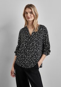 Blusa nera a maniche lunghe con un motivo geometrico bianco. Caratterizzata da un colletto a V e maniche gather. Tessuto morbido e leggero.