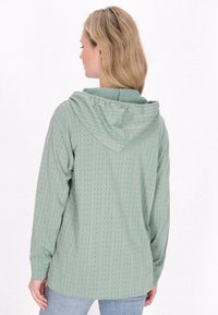 Felpa verde chiaro con un motivo a trecce testurizzate, maniche lunghe e cappuccio con coulisse. Il design presenta una vestibilità rilassata e una schiena arricciata.