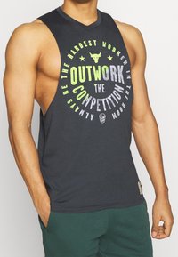 Camiseta sin mangas de color gris oscuro con texto multicolor en negrita que dice "SUPERA A LA COMPETENCIA", con un logo de toro y costuras en contraste.
