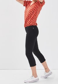 Haut à col en V à motifs floraux rouges, jeans noirs cropped, baskets blanches. Le t-shirt a des manches courtes. Les jeans ont une coupe ajustée avec des poches arrière.