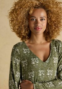 Zelené šaty s kvetinovým vzorom, výstrihom do V a dlhými rukávmi, s precízne vyšívanými bielymi kvetmi a mäkkou, textúrovanou látkou.