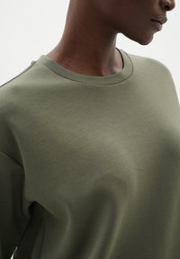 Olivově zelená bavlněná mikina s kulatým výstřihem, hladkou texturou a uvolněným střihem, disponující minimálním šitím a bez viditelného kování.