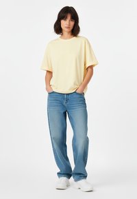 Lichtgele t-shirt met korte mouwen en een relaxte pasvorm, gecombineerd met rechte, blauwe jeans en witte sneakers. Eenvoudig en casual ontwerp.