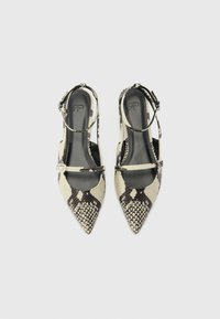Zapatos de tacón tipo slingback con puntera afilada en estampado de serpiente en crema y negro. Material sintético texturizado con una delgada correa para el tobillo y detalle de hebilla.