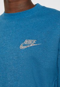 Felpa blu realizzata in tessuto morbido, con un logo Nike argentato scintillante sul petto e design a collo rotondo.