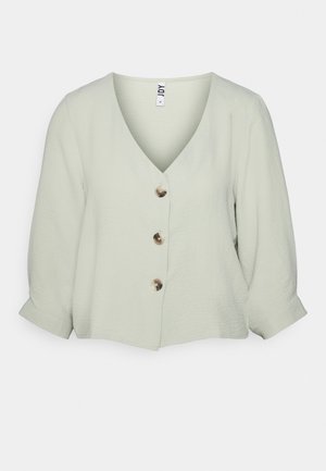 Blouse vert clair en V avec trois gros boutons sur le devant et manches trois-quarts avec poignets.