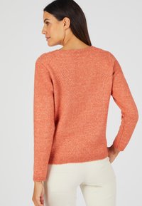 Pull en tricot orange avec des manches longues et un col rond. Texture lisse et ourlet côtelé, avec des détails subtils au niveau des épaules.