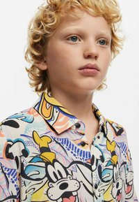 Camicia button-up multicolore con un design di cartoni animati giocoso, caratterizzata da illustrazioni prominenti di personaggi su uno sfondo chiaro.