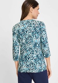 Bloemmotief, driekwart mouw top in tinten blauw en teal, lichte stof met een soepele textuur en ronde halslijn.