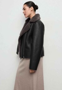 Czarna skórzana kurtka o dwurzędowym kroju z miękkim, szarym futrzanym kołnierzem, z krótkim fasonem i srebrnym zamkiem błyskawicznym.