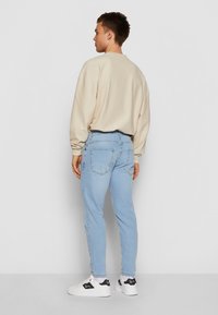 Šviesiai smėlio spalvos ribuotas megztinis, šviesiai mėlyni siaurėjantys džinsai, balti sportbačiai su juodais akcentais, matomi iš nugaros. Paprastas, modernus dizainas.