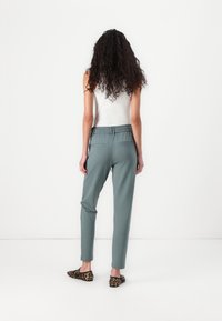 Helle grüne, elastische Hosen mit schmalem Bein, ausgestattet mit zwei Gesäßtaschen, kombiniert mit flachen Schuhen im Leopardenmuster.