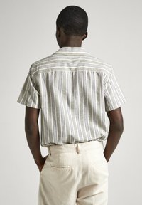 Kortärmad skjorta med knappar och vertikala ränder i beige, grå och lavendel; lätt tyg; ryggdetalj; kombinerad med ljusa byxor.
