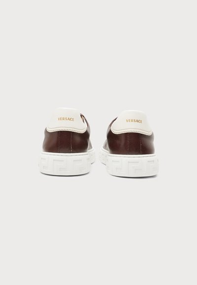 Paire de baskets en cuir marron Versace avec talons blancs et semelle blanche épaisse à motif, vue de dos sur un fond uni.