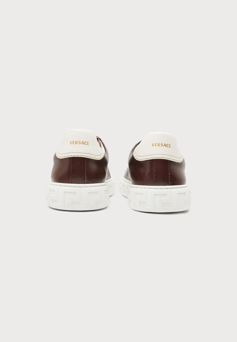 Pair of brown leather Versace sneakers with white heels and thick white patterned sole, viewed from the back on a plain background.