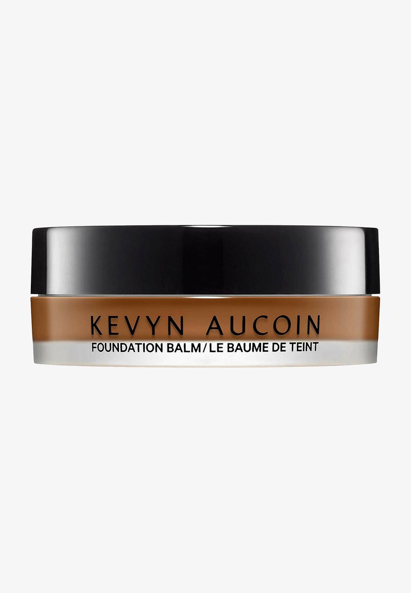 Fundamentbalsam in einem runden Glas, mit einem schwarzen Deckel und einem beige-braunen Körper mit klarem Boden. Der Text enthält "Kevyn Aucoin" und den Produktnamen.