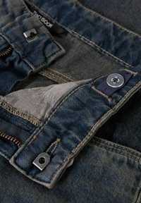 Tela de mezclilla de color azul oscuro. Presenta una cremallera y botones plateados, junto con costuras visibles y un forro interior gris sólido.