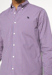 Karierte Hemd mit einem lila und rosa Gingham-Muster, Button-Down-Kragen und kleinem gesticktem Logo auf der Brust.