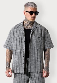 Kurzärmliges, knöpfbares Hemd aus schwarz-weiß gestreiftem Stoff, mit einer Tasche auf der linken Seite und einer lockeren Passform.