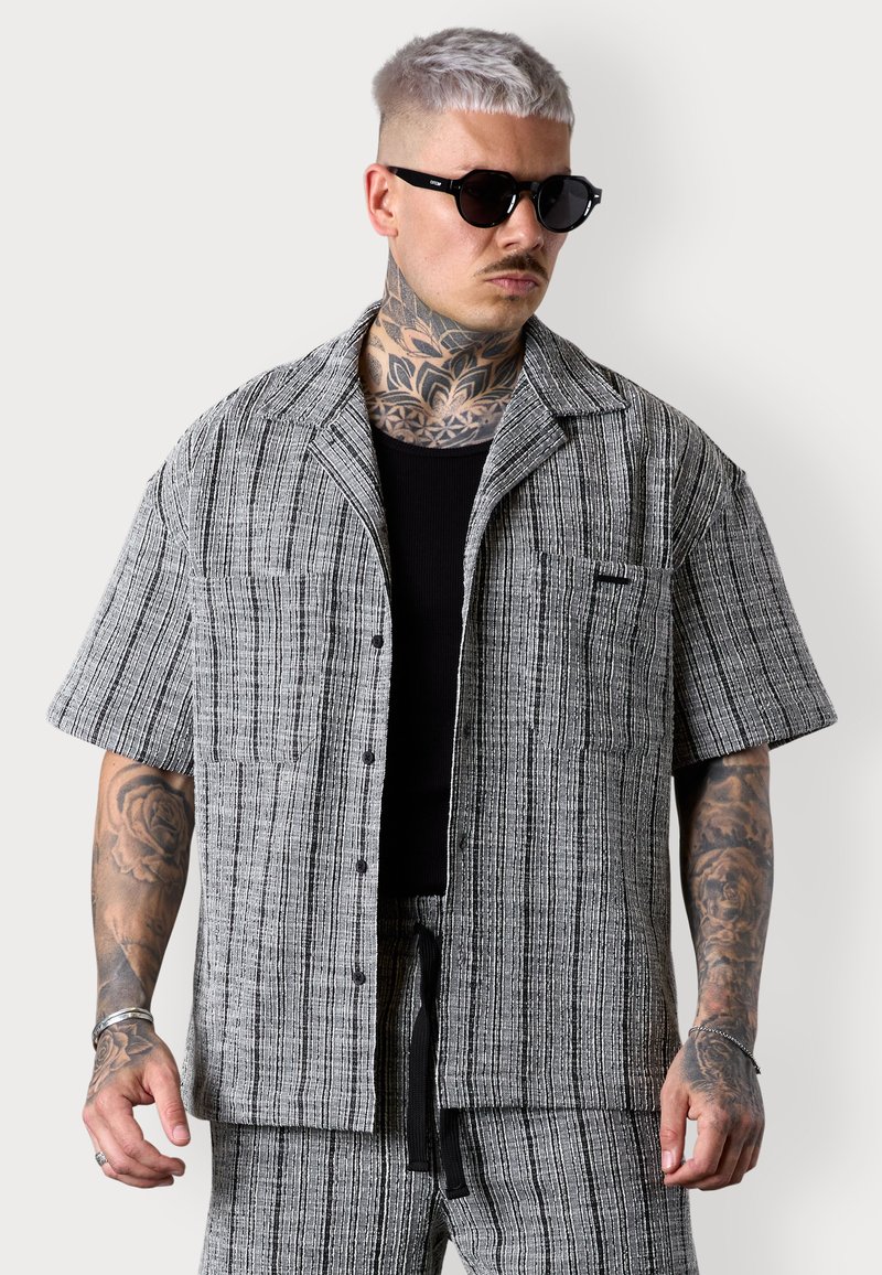 Kurzärmliges, knöpfbares Hemd aus schwarz-weiß gestreiftem Stoff, mit einer Tasche auf der linken Seite und einer lockeren Passform.
